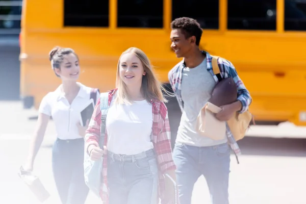 Grupo de estudiantes adolescentes felices caminando frente al autobús escolar - foto de stock
