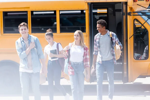 Groupe de jeunes chercheurs marchant ensemble devant le bus scolaire — Photo de stock