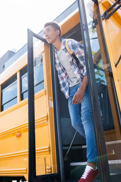 Vista inferiore di felice teen africano americano scolaro a piedi fuori scuolabus — Foto stock