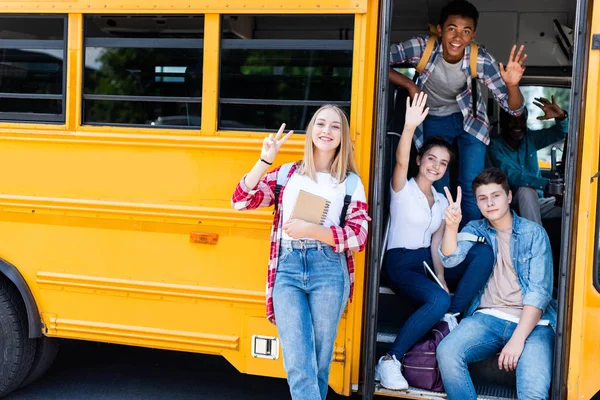 Gruppe von Teenagern sitzt am Schulbus mit Fahrer drinnen und zeigt verschiedene Gesten in die Kamera — Stockfoto