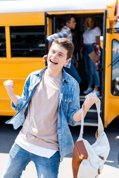 Celebrating teen schoolboy running out of school bus with blurred classmates on background — Stock Photo