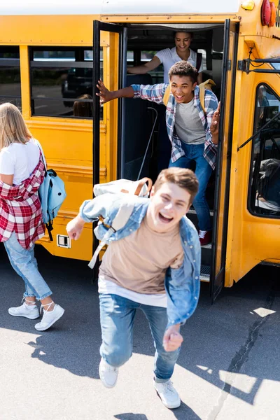 Grupo de jóvenes eruditos felices corriendo en la escuela desde el autobús - foto de stock