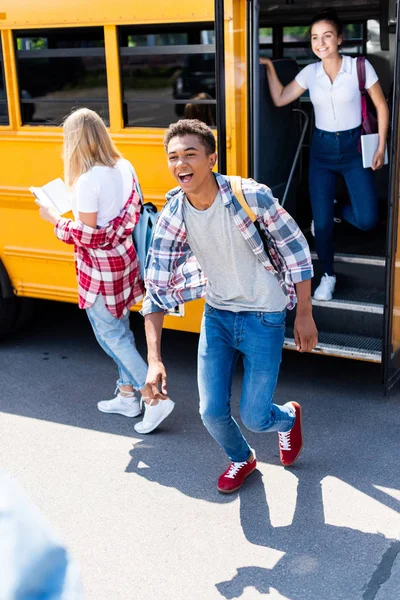 Riéndose afroamericano escolar corriendo fuera de la escuela autobús con compañeros de clase - foto de stock
