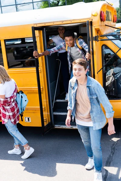 Grupo de estudiantes adolescentes que corren en la escuela desde el autobús - foto de stock