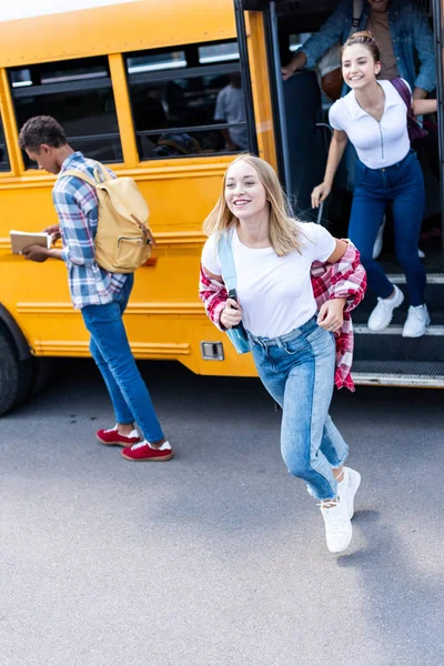 Sonriendo multiétnicos adolescentes eruditos corriendo fuera de autobús escolar - foto de stock