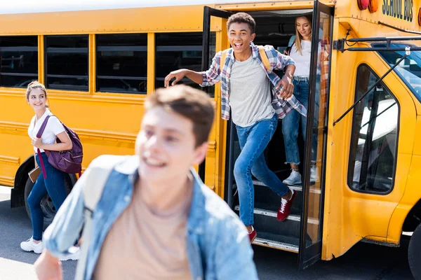 Grupo de jóvenes eruditos felices corriendo fuera de autobús escolar - foto de stock