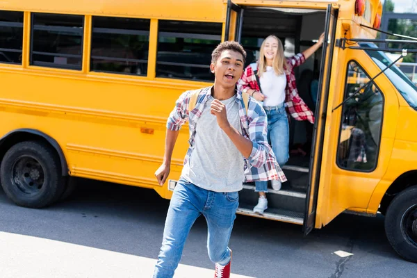 Multiétnicos adolescentes estudiantes pareja corriendo fuera de autobús escolar - foto de stock