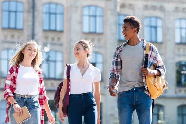 Group of multiethnic teenagers with backpacks having walk together with old school building on background — Stock Photo