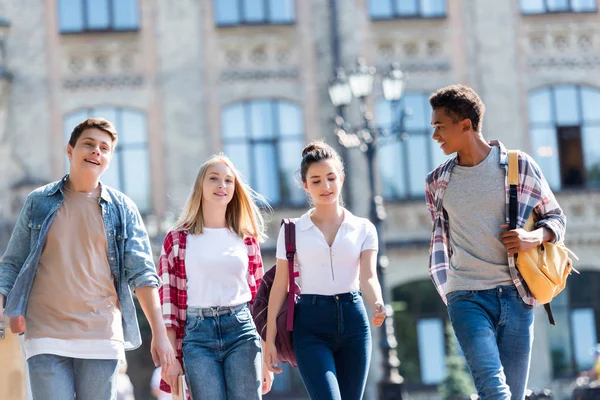 Group of happy multiethnic teenagers with backpacks having walk together — Stock Photo