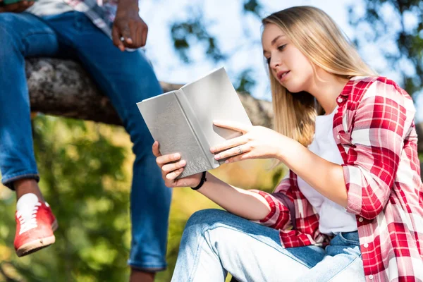 Cropped shot of teen students couple reading books while sitting on tree — Stock Photo