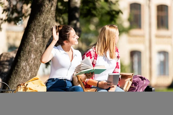 Teenager-Schulmädchen sitzen auf Bank und lesen gemeinsam Hausaufgaben — Stockfoto