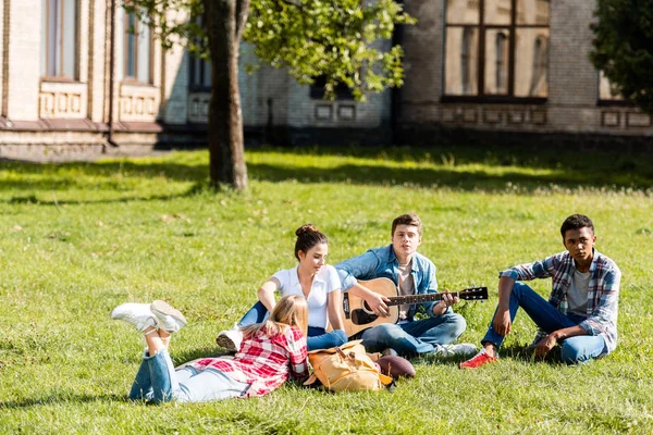 Groupe d'adolescents passer du temps ensemble et écouter des chansons de guitare sur l'herbe — Photo de stock