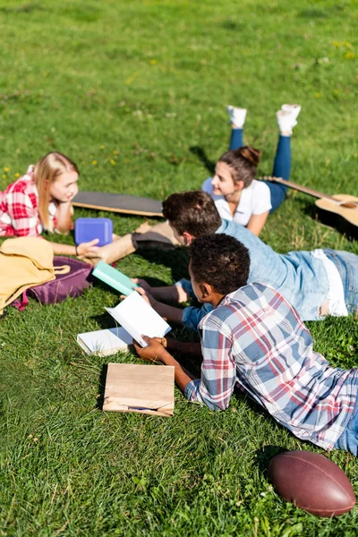 Grupo de adolescentes eruditos acostados en la hierba y estudiando juntos - foto de stock