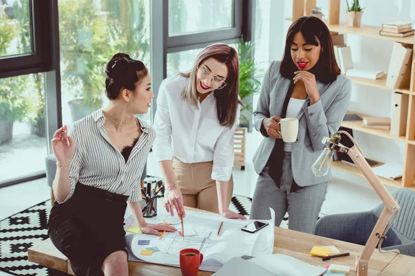 Groupe multiethnique de jeunes femmes d'affaires travaillant avec le plan directeur et buvant du café au bureau — Photo de stock