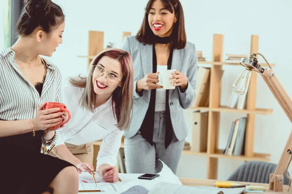 Grupo multiétnico de jóvenes empresarias que trabajan con el proyecto y toman café en la oficina - foto de stock