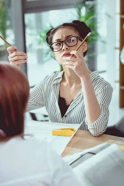 Pensive asian businesswoman in eyeglasses holding pencils and looking up — Stock Photo