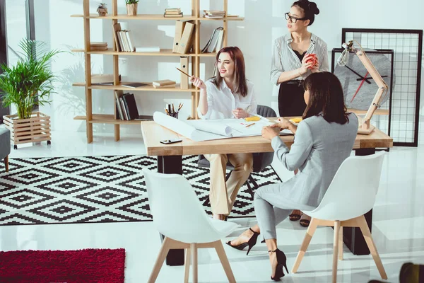 Groupe multiethnique de jeunes femmes d'affaires travaillant avec des plans et discutant de nouveaux projets — Photo de stock