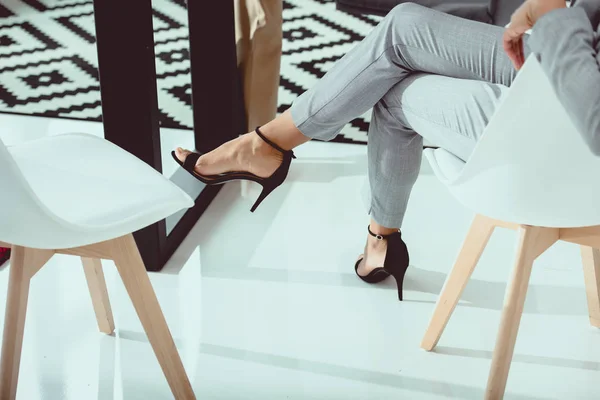 Cropped shot of businesswoman in suit and high heeled shoes sitting in chair in office — Stock Photo