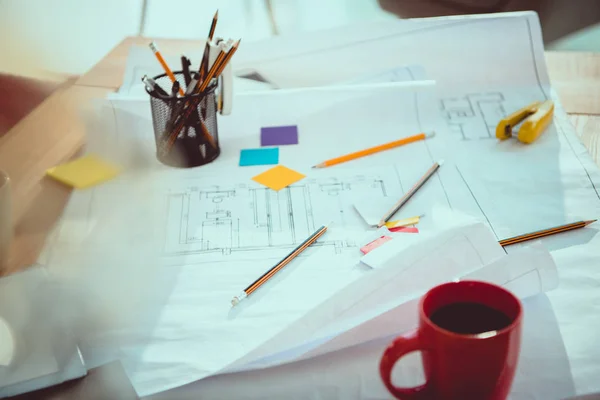 Close-up view of various office supplies, coffee cup and blueprints on office table — Stock Photo