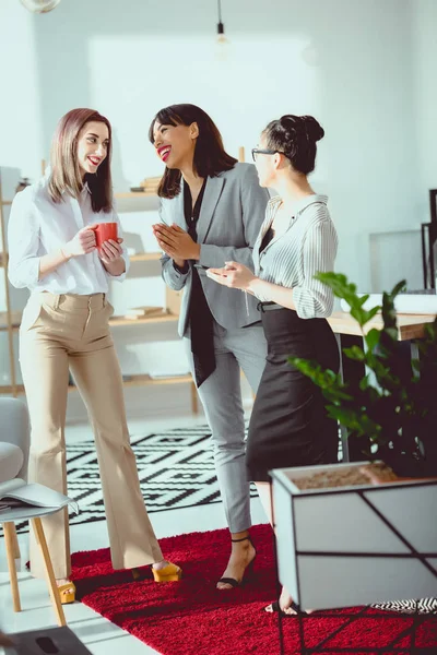 Jóvenes empresarias multiétnicas tomando café y hablando en la oficina - foto de stock