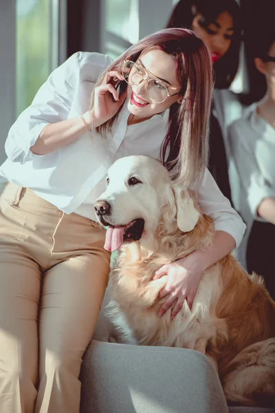 Усміхнена біла бізнес-леді розмовляє на смартфоні і обіймає собаку — стокове фото