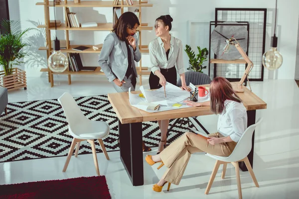 Jóvenes arquitectos multiétnicos que trabajan con planos en la oficina moderna - foto de stock