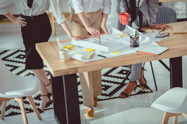 Fotografía recortada de arquitectos en ropa formal trabajando con planos en la mesa - foto de stock