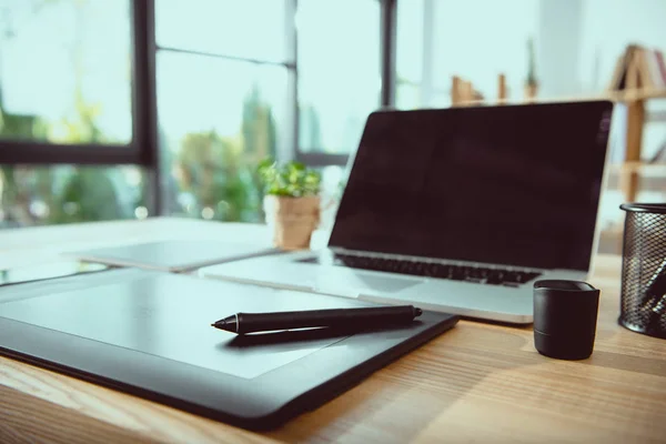 Computer portatile con schermo bianco e tablet grafico su tavolo in legno in ufficio — Foto stock