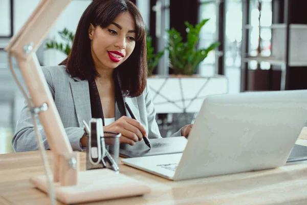 Junge afrikanisch-amerikanische Designerin arbeitet im Büro mit Tablet und Laptop — Stockfoto