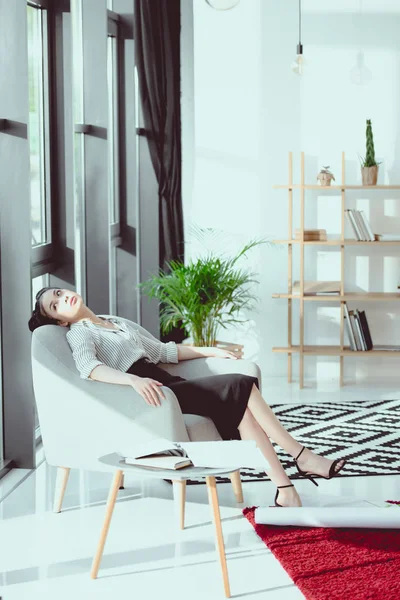Cansado joven asiático mujer de negocios relajarse mientras sentado en sofá en oficina - foto de stock