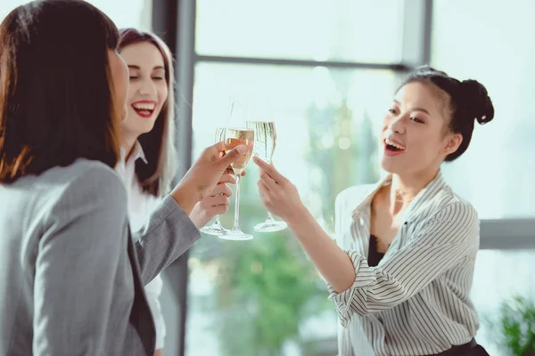 Glückliche multiethnische Geschäftsfrauen, die mit Champagnergläsern klirren und lächeln — Stockfoto