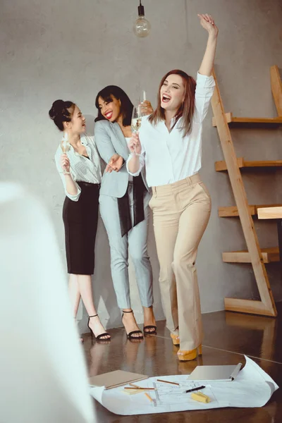 Jeunes femmes d'affaires multiethniques célébrant le succès et buvant du champagne à l'intérieur — Photo de stock