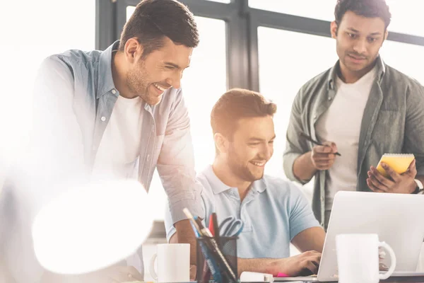 Lächelnde junge multiethnische Geschäftsleute mit Laptop und Notizen im Büro — Stockfoto