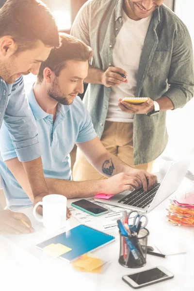 Schnappschuss fröhlicher junger Geschäftsleute mit Laptop und Notizen im Büro — Stockfoto