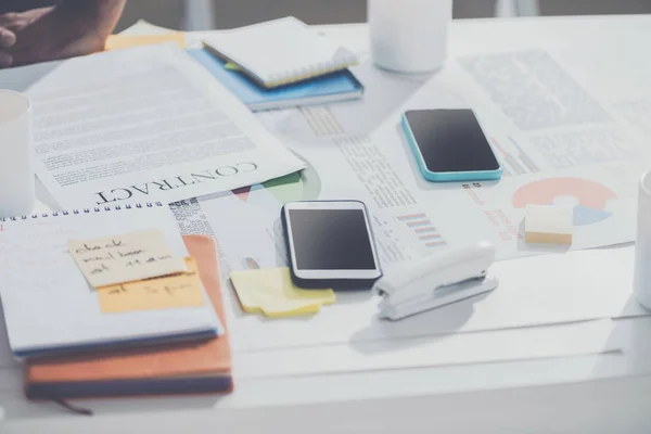 Smartphones com contrato e notebooks com grampeador na mesa no escritório moderno, estabelecimento de negócios — Fotografia de Stock