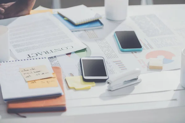 Teléfonos inteligentes con contrato y portátiles con grapadora en la mesa en la oficina moderna, establecimiento de negocios - foto de stock