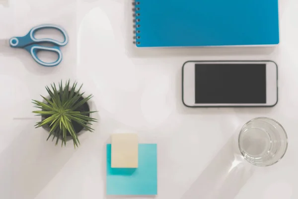 Smartphone von oben mit leerem Bildschirm, grüner Pflanze, Wasserglas, Schere, Notizbuch und Haftnotizen am Arbeitsplatz — Stockfoto