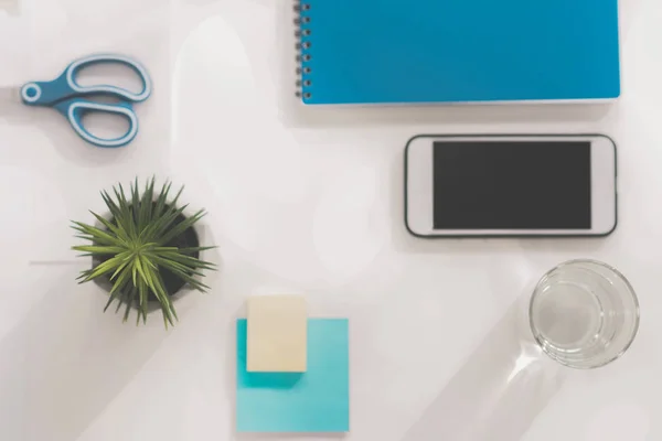 Top view of smartphone with blank screen, green plant, glass of water, scissors, notebook and sticky notes at workplace — Stock Photo