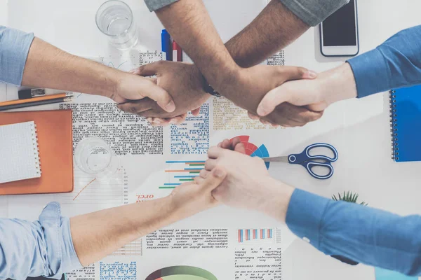 Vista superior de los hombres de negocios sentados en la mesa con papeles y estrechando las manos, concepto de trabajo en equipo de negocios - foto de stock