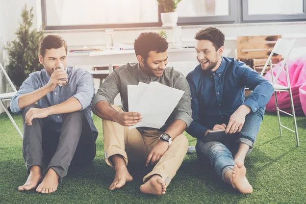 Souriant jeunes hommes d'affaires pieds nus assis avec des papiers et en utilisant une tablette numérique, concept de travail d'équipe d'affaires — Photo de stock