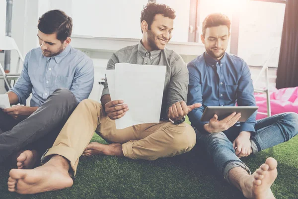 Souriant jeunes hommes d'affaires pieds nus assis avec des papiers et en utilisant une tablette numérique, concept de travail d'équipe d'affaires — Photo de stock