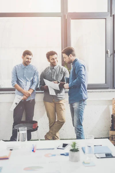 Три молодых бизнесмена, стоящих вместе и обсуждающих документы, концепцию совместной работы — стоковое фото