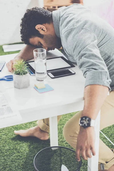 Joven hombre de negocios afroamericano durmiendo sobre la mesa en la oficina moderna - foto de stock