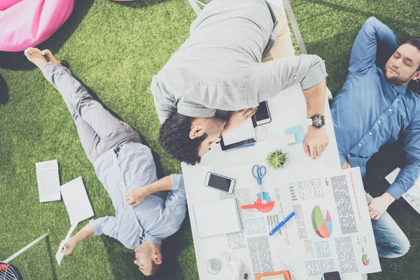 Young businessmen sleeping on the table and green grass carpet at modern office, business teamwork — Stock Photo