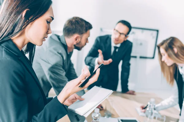 Junge asiatische Geschäftsfrau schaut auf Notizbuch, während sie Gespräche hört — Stockfoto