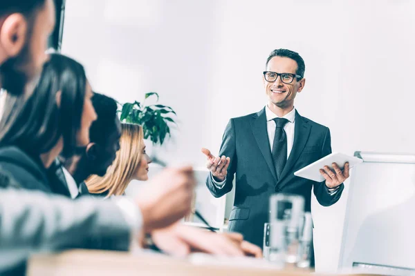 Happy handsome team leader with tablet talking to multiracial managers in conference hall — Stock Photo