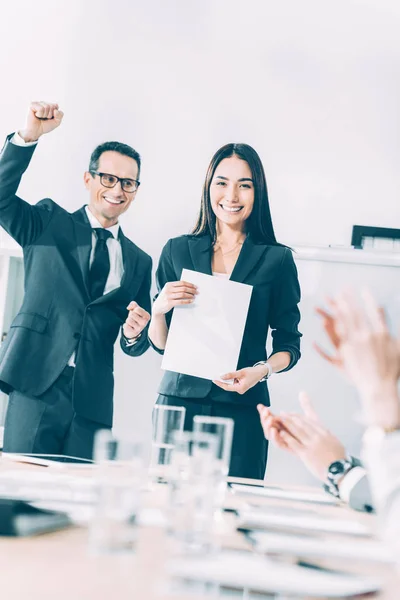 Recompensado joven asiático la gerencia holding en blanco papel mientras colegas aplaudiendo a su - foto de stock