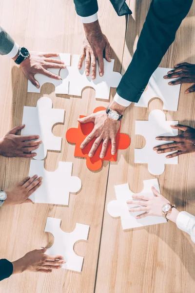 Overhead view of multiracial businesspeople assembling puzzle on table — Stock Photo
