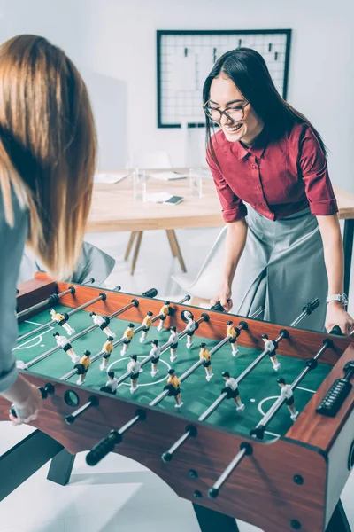 Jóvenes y atractivas empresarias jugando futbolín en la oficina moderna - foto de stock