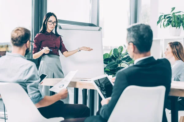 Joven asiático mujer de negocios dando presentación a multirracial colegas en conferencia sala - foto de stock